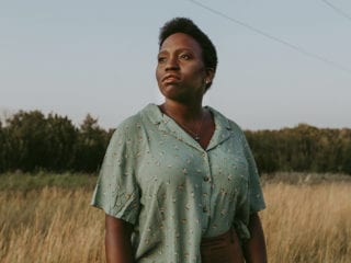 A black woman with short hair standing in a field looking in the distance