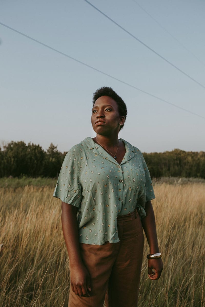 A black woman with short hair standing in a field looking in the distance