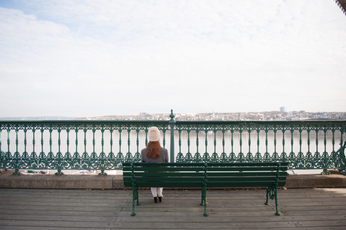 A woman sitting on a bench looking out onto the water and cityscape