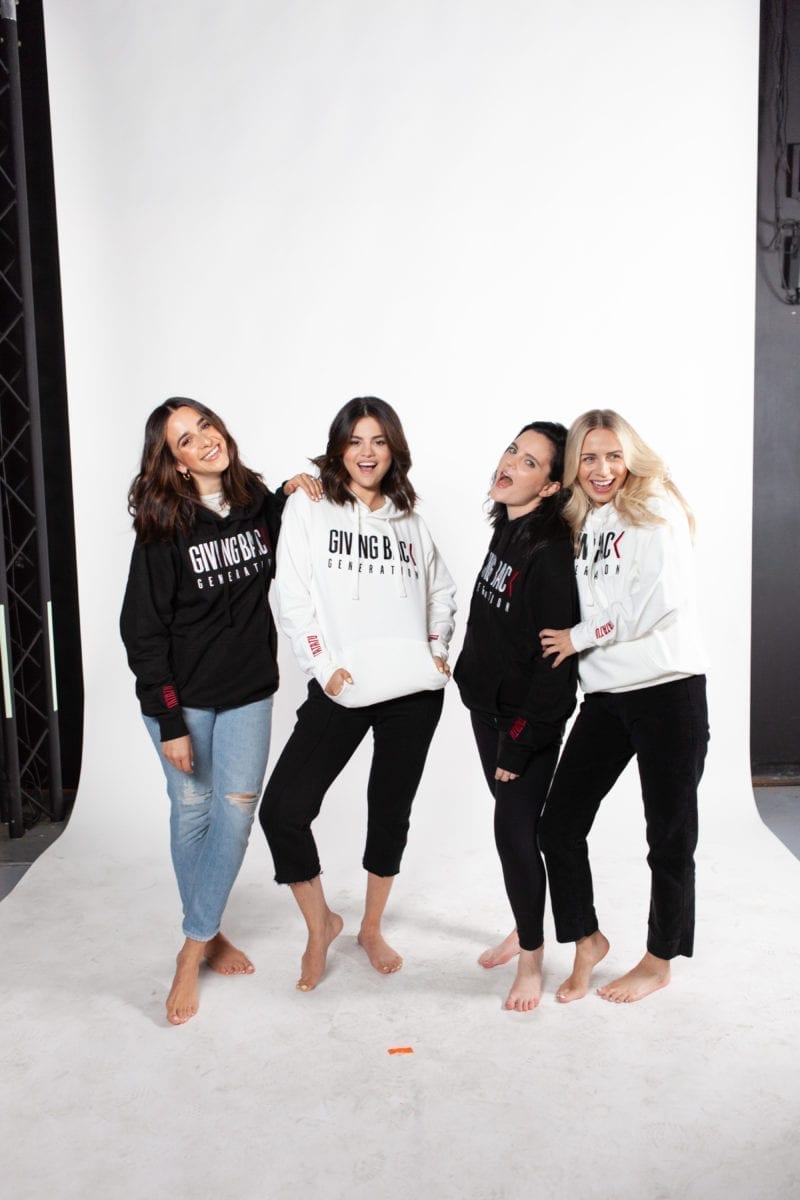 Four women in hoodies standing and smiling and laughing toward the camera