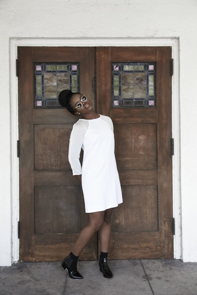 A woman in a white dress and sunglasses standing in front of wooden doors