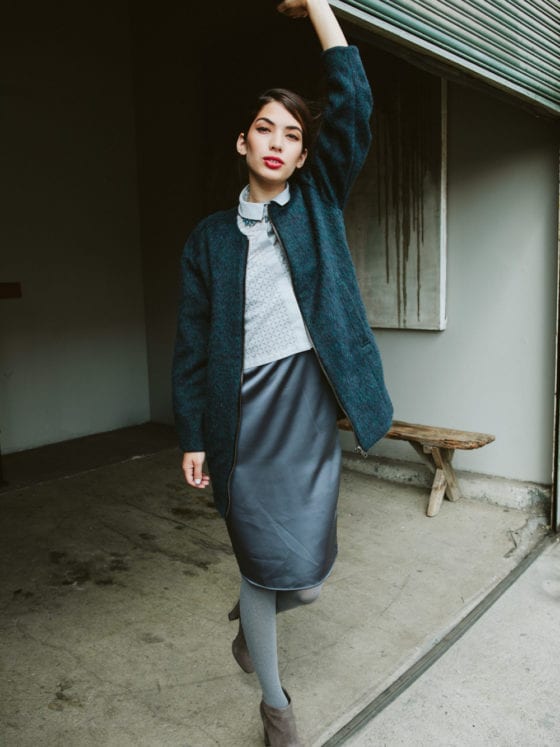 A woman in a sweater and skirt holding up a garage door while staring at the camera