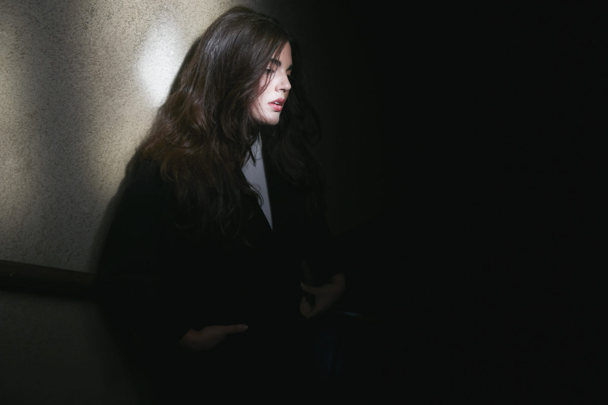 A woman in a dark room wearing a dark sweater and looking down