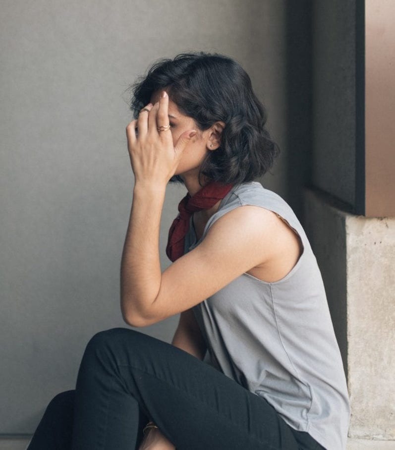 Woman sitting on the floor by a wall with her hand touching her face