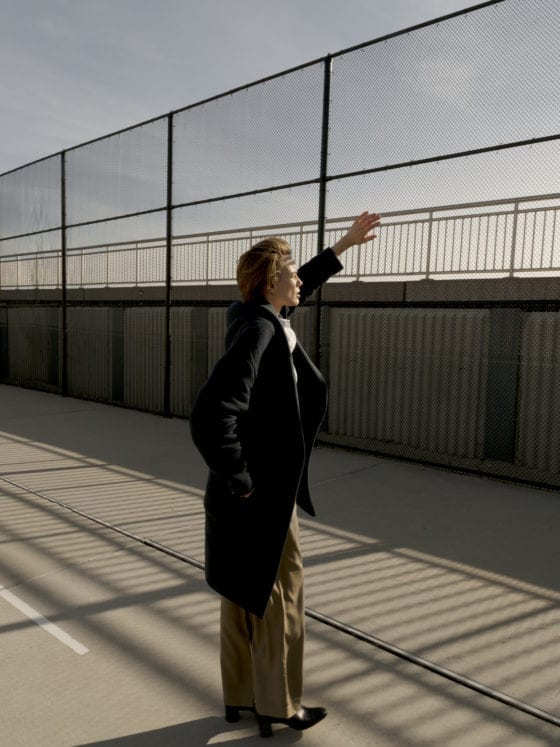 A woman standing looking through a wired fence