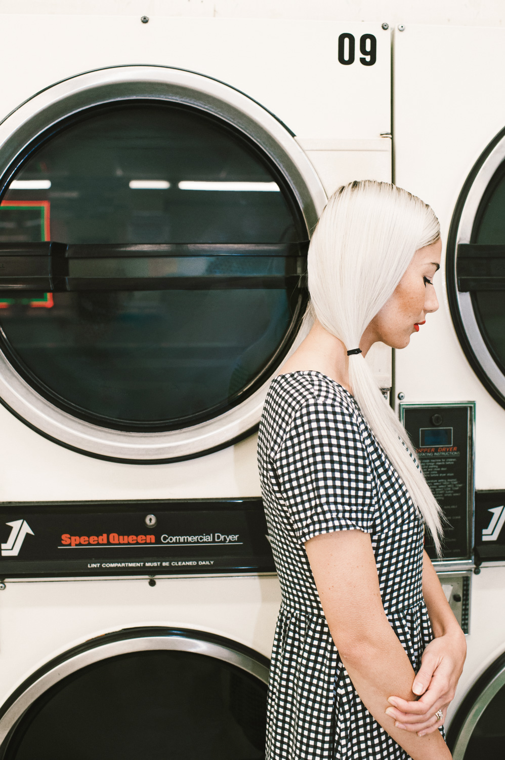 A woman standing next to a washer/dryer at the laundry mat
