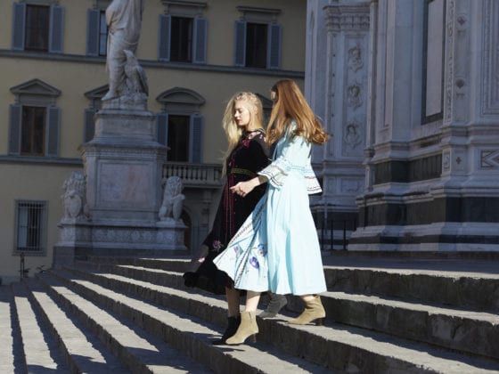 Two women walking down the stairs in dresses and their hair blowing