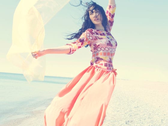 A woman standing on the beach dancing with a flow scarf