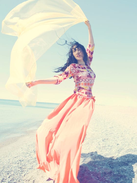 A woman standing on the beach dancing with a flow scarf