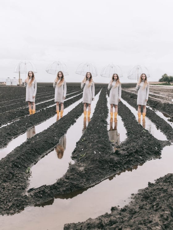Five identical woman standing in the trenches of a field with umbrellas