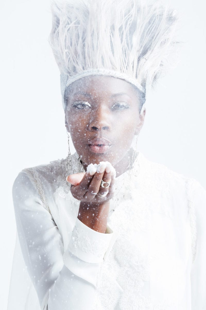 A woman wearing an all white outfit and white hat blowing snow
