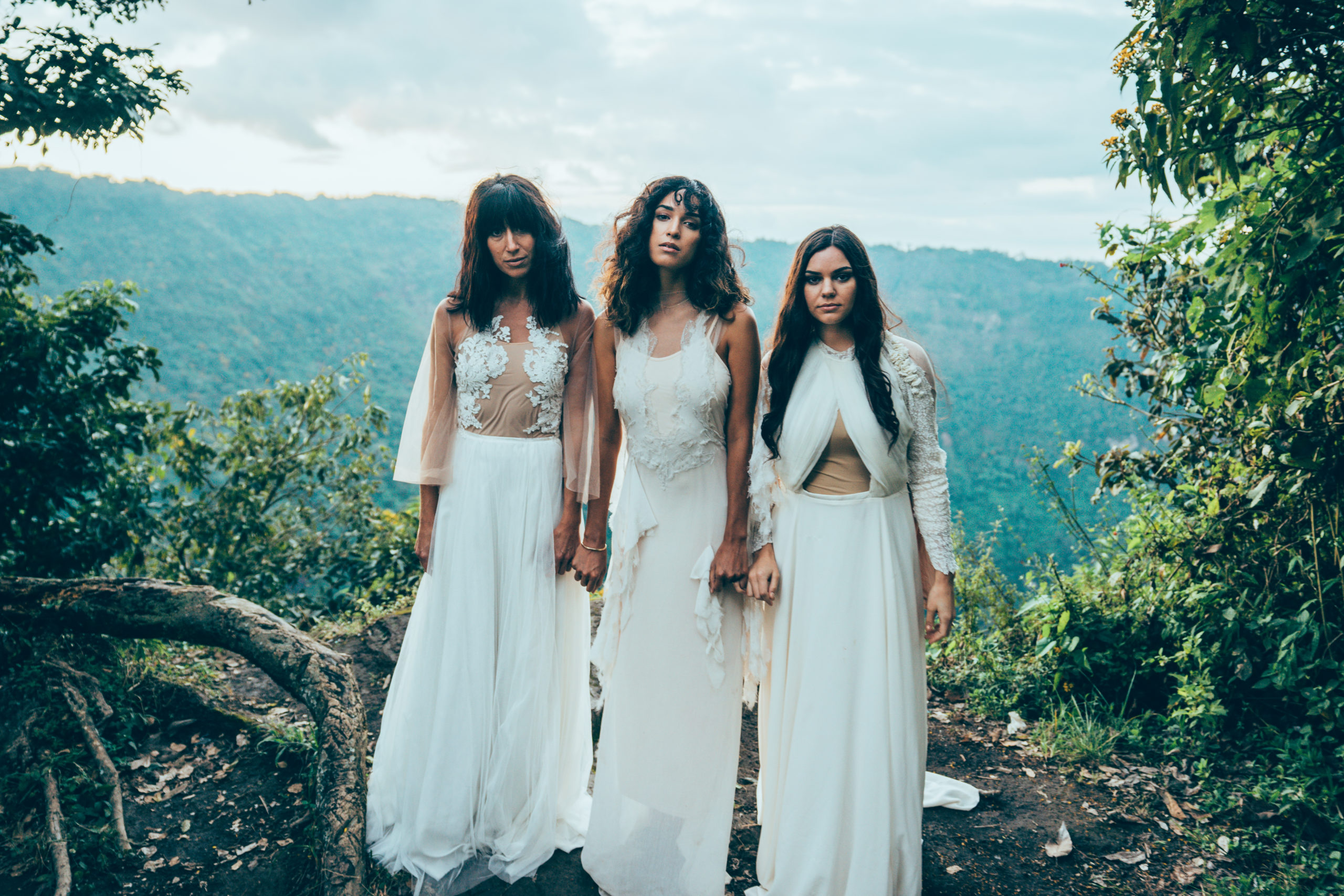 Three women in white dresses holding hands on the side of a mountain