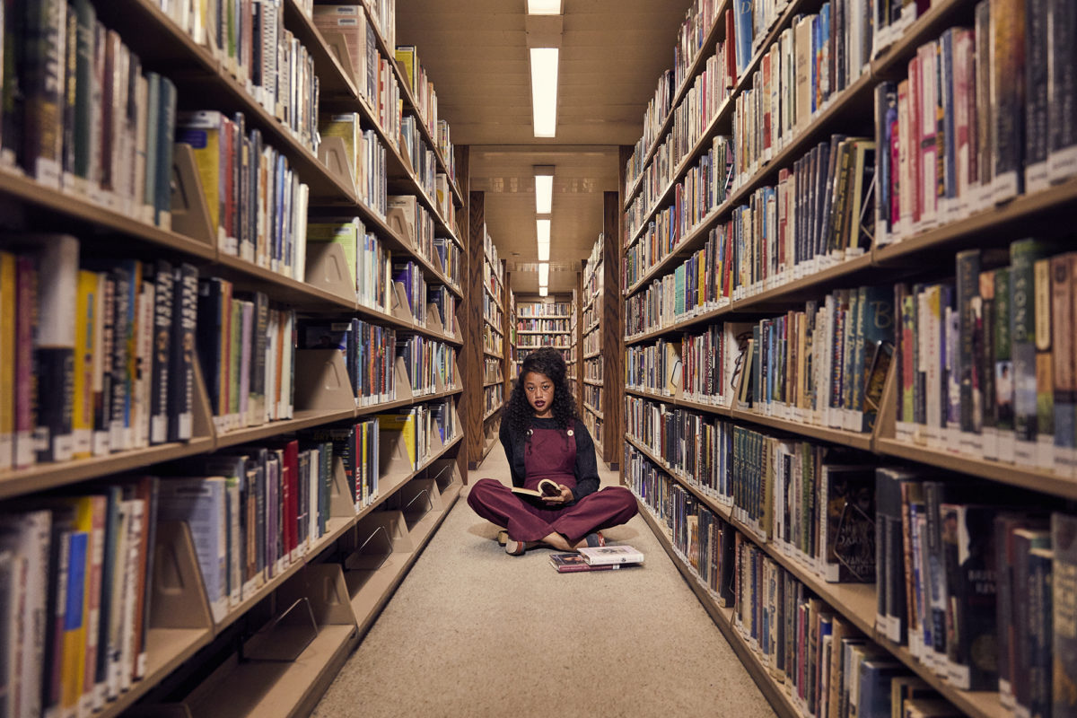 A girl sitting on the floor of a library between book cases
