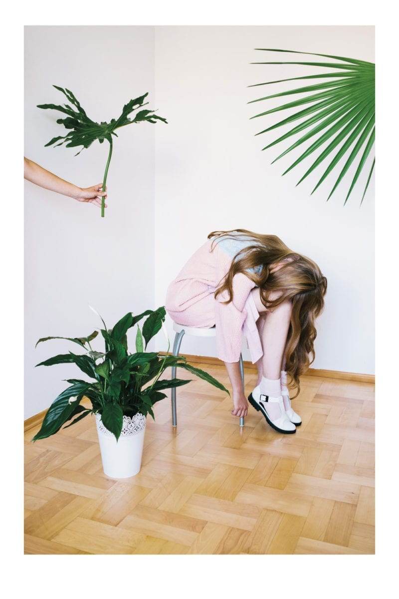 A woman bent over in a chair with her hair falling over her face as a hand holds a plant toward her
