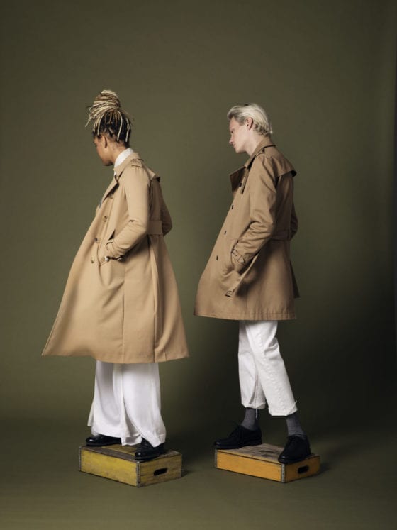 A man and woman standing dressed in trench coats stepping on wooden crates