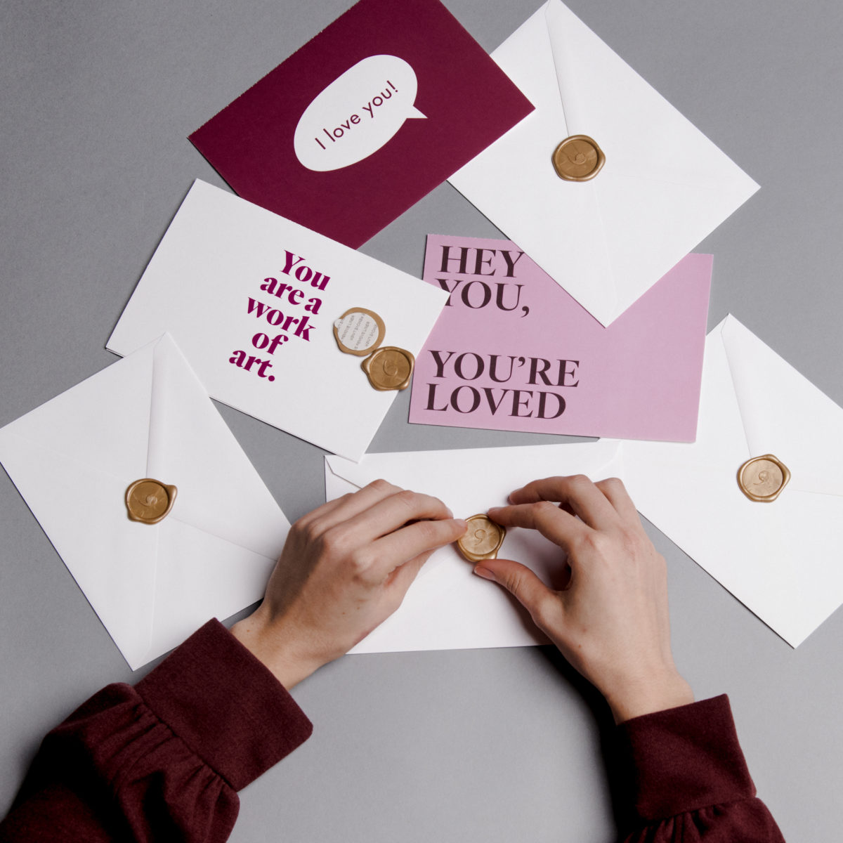 Hands touching a wax seal on an envelope atop of a stack of cards and envelopes