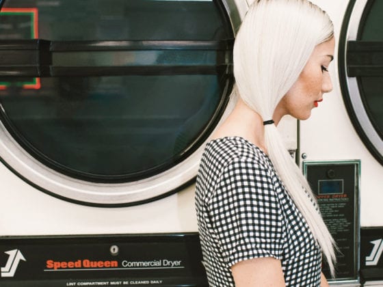 A side profile of a woman with her hair in pigtails standing in front of a washer at a laundry mat
