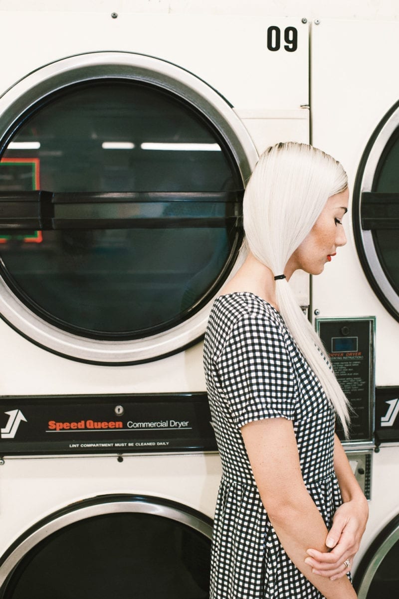 A side profile of a woman with her hair in pigtails standing in front of a washer at a laundry mat