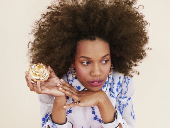 A woman holding a donut in one hand with the other underneath her chin