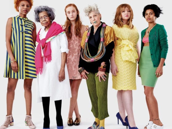 A group of diverse women in multiple bright colors standing and staring in the camera without smiles