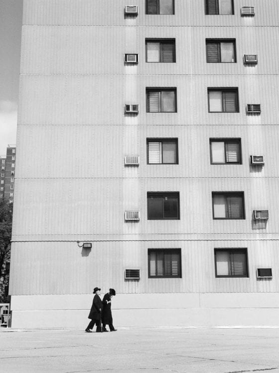 Two men in long jackets and black hats walking by a building