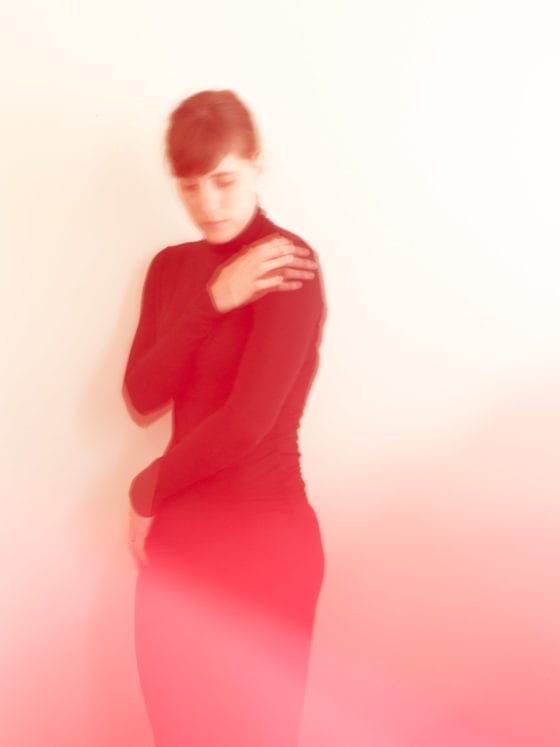 A blurry image of a woman in all black as she wraps her arms around herself