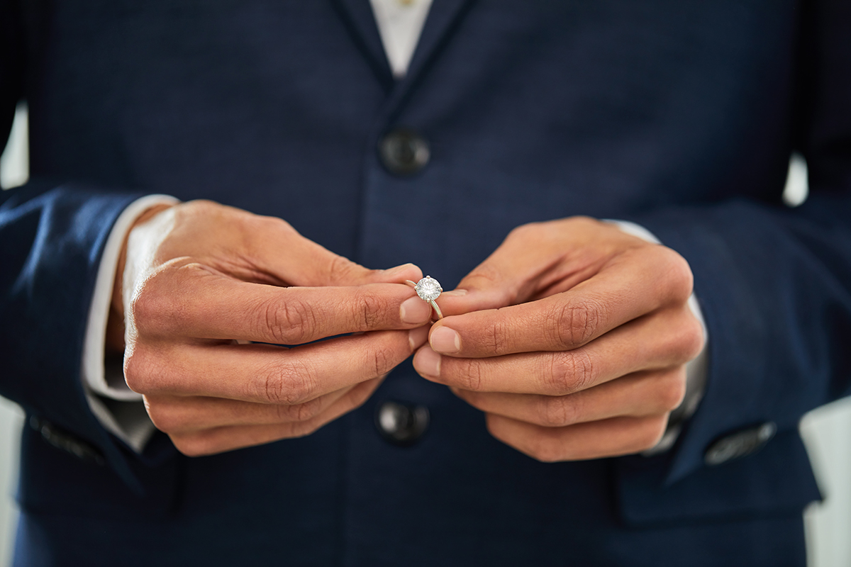 A close up of a man's hands holding a diamond ring