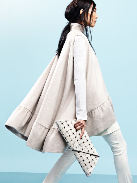 A side profile of a woman with a cape jacket and a hand purse