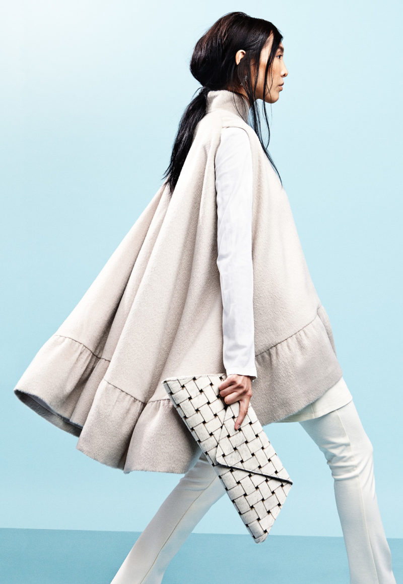 A side profile of a woman with a cape jacket and a hand purse