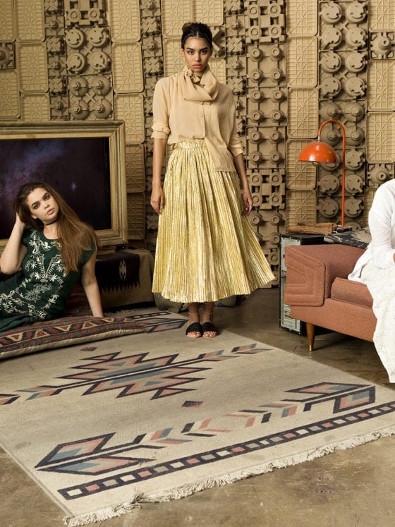 A group of three woman in a small living room, one seated on the couch, another on the floor and one standing
