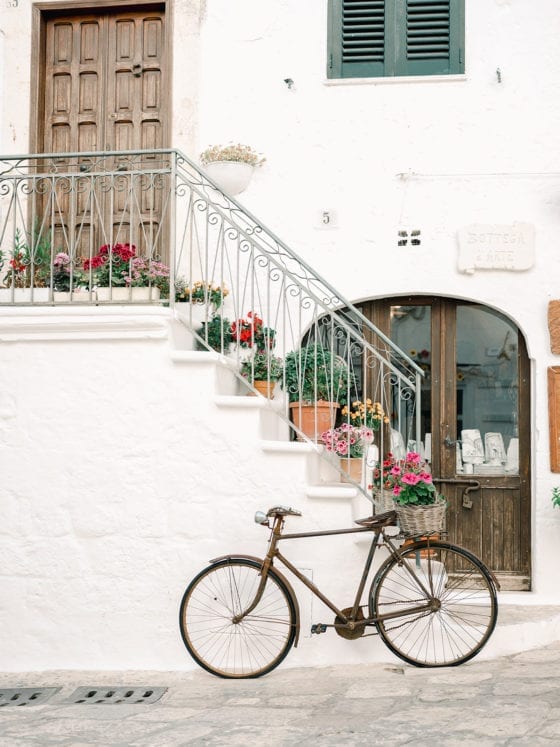 A bike leaning against the outside stairs to a building with flower pots lining the steps