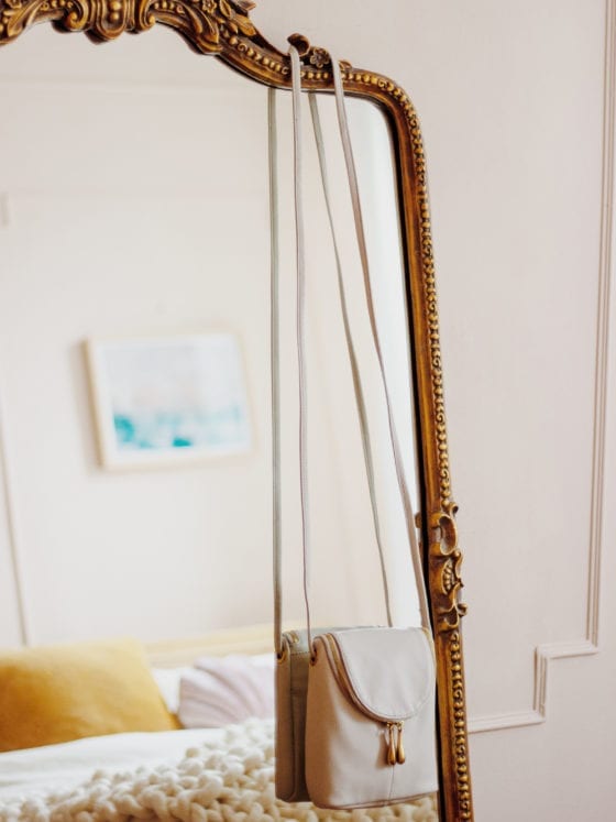 A purse hung over the side of a full-length mirror