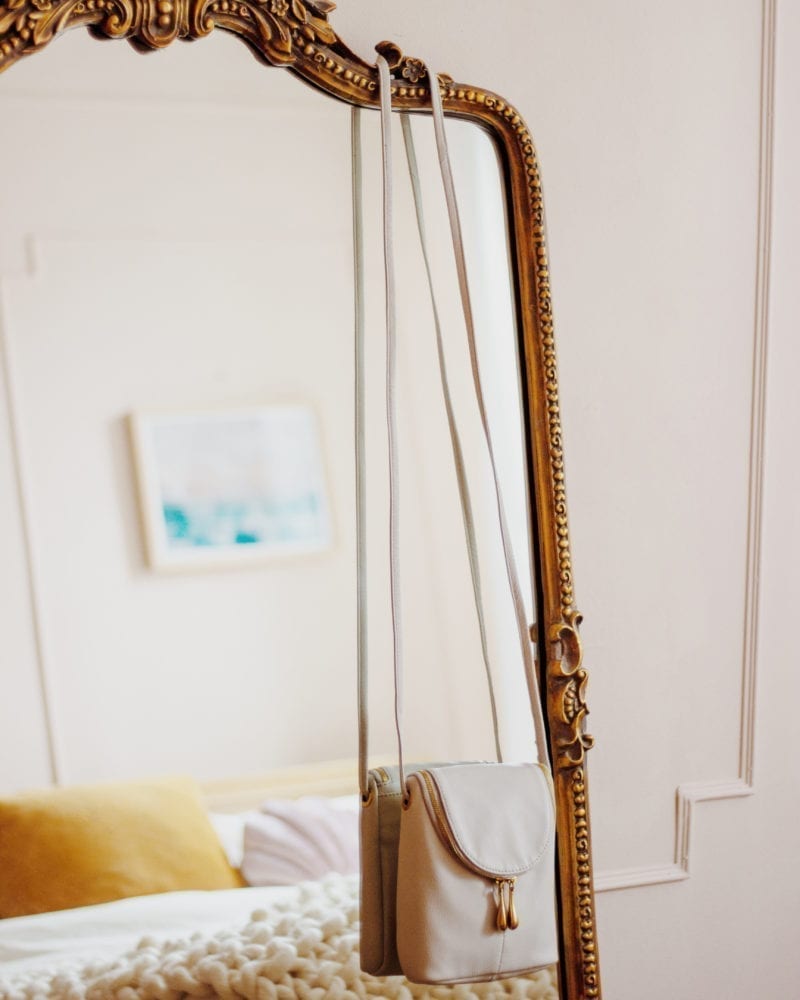 A purse hung over the side of a full-length mirror