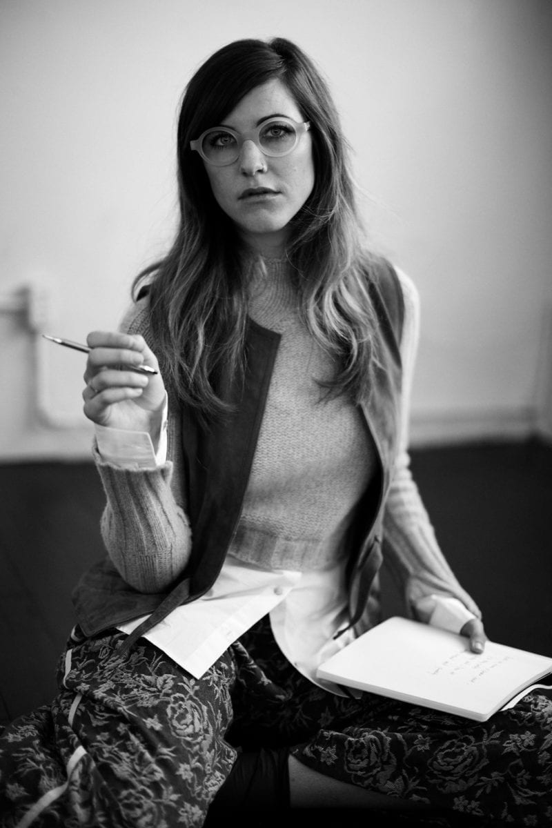 A girl with glasses holding a notebook and a pencil in her hand