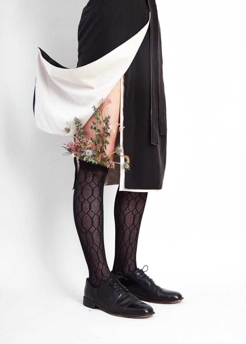 A woman's skirt pulled up to expose her knee high socks that have flowers sprouting out of them