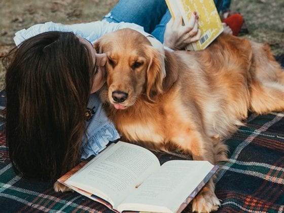 A woman lying on a blanket next to her dog as she reads