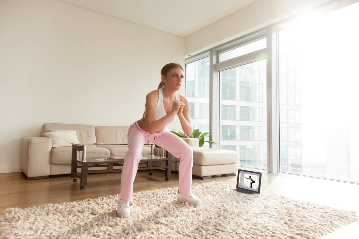 A woman doing a squat in her home as she works out with a video recording