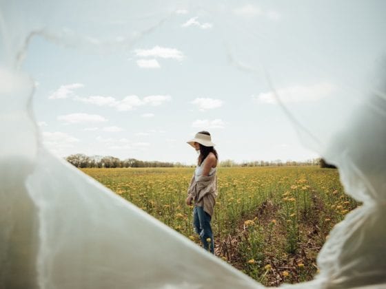 A woman standing in a field of sunflowers with a ripped plastic wrap covering the frame of the camera