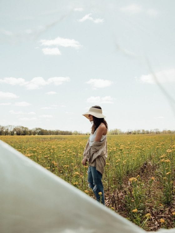 A woman standing in a field of sunflowers with a ripped plastic wrap covering the frame of the camera