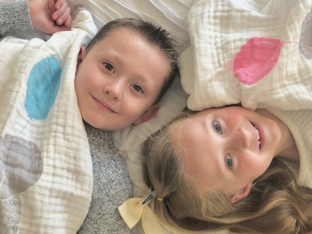 A little boy and girl lying down with blankets on top of them