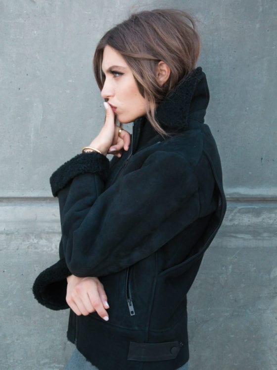 A side profile of a woman in a black sweater with her thumb pressed against her lip
