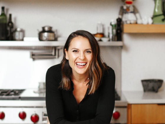 A woman smiling as she leans over a kitchen counter