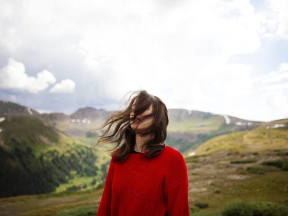 A woman looking onward as her hair blows across her face with mountains in the background