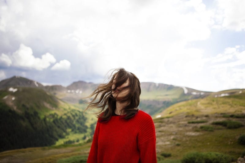 A woman looking onward as her hair blows across her face with mountains in the background