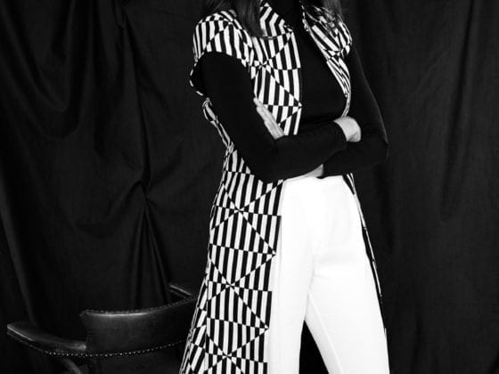 A black and white photo of a woman in white pants standing in front of a black background