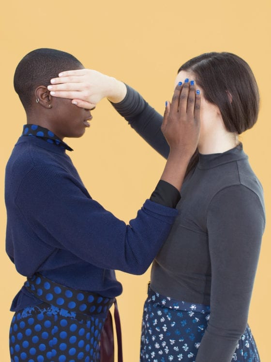 A picture of a white woman and a black woman covering each other's faces