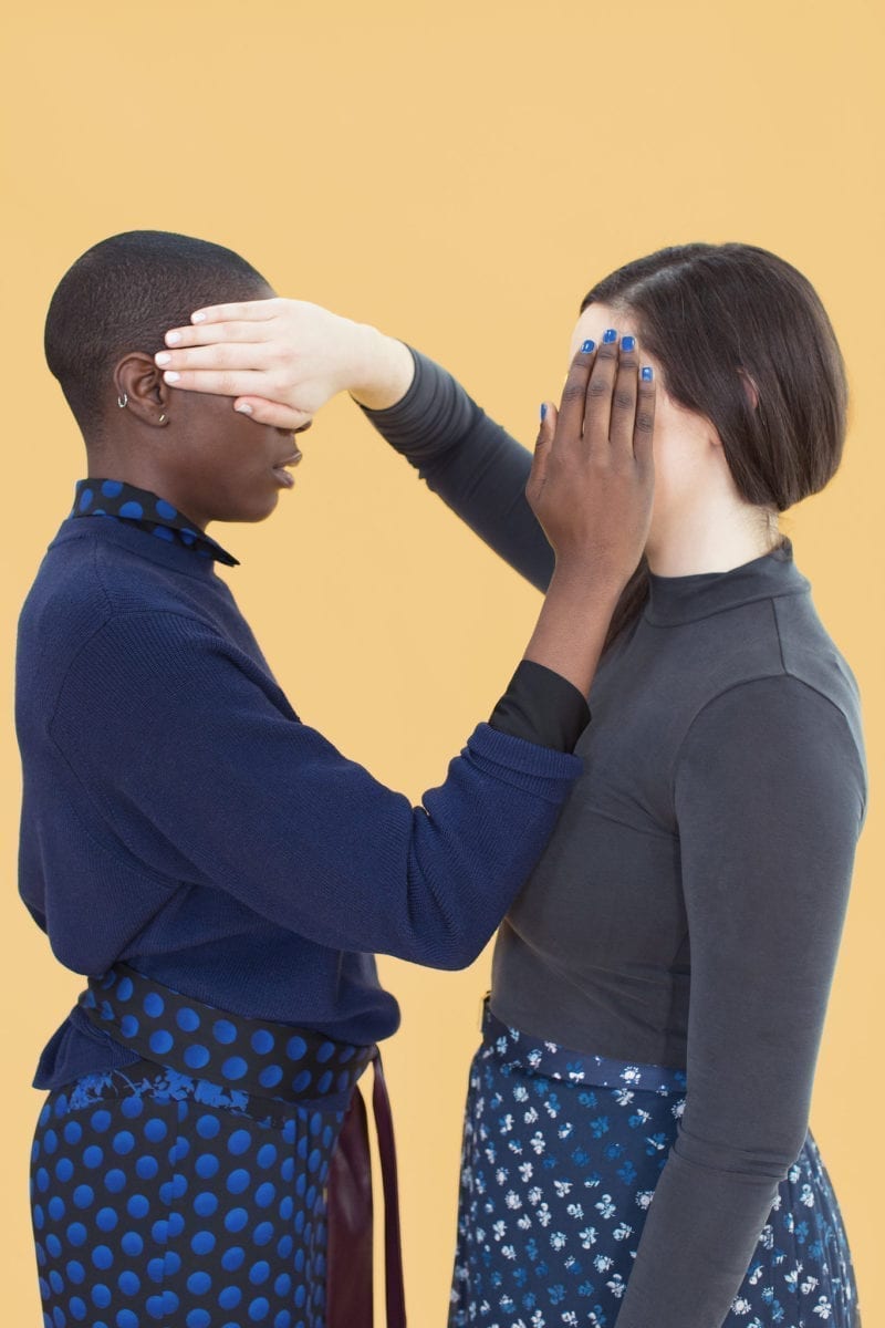 A picture of a white woman and a black woman covering each other's faces