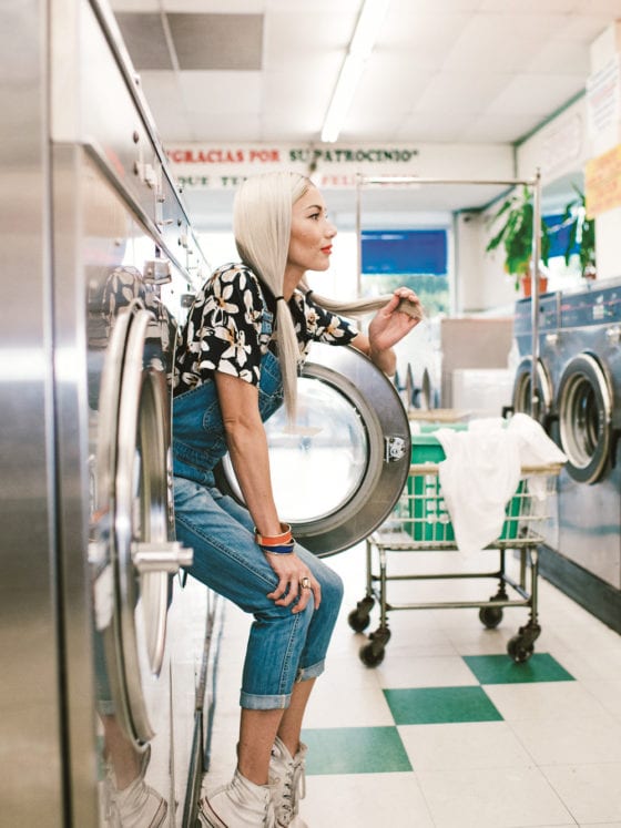 A woman siting on the edge of a washer machine that isn't on