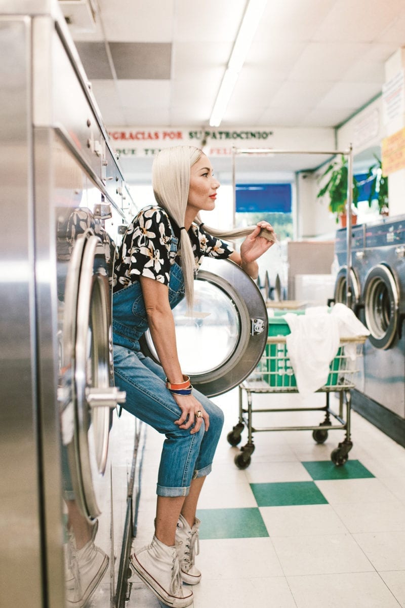 A woman siting on the edge of a washer machine that isn't on