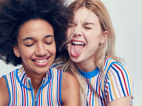 Two smiling girls with their eyes closed as one sticks her tongue out and the other laughs